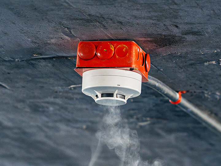 White smoke detector on red electrical box on the ceiling of a carport parking lot