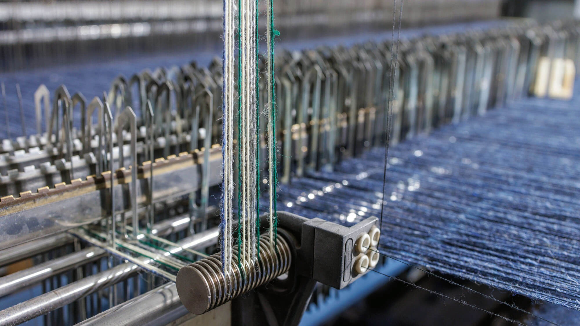 Closeup of indigo warp threads on a modern weaving machine showing precision denim manufacturing and automated textile production.