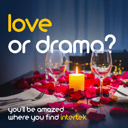 Two wine glasses next to a candle on a table adorned with rose petals